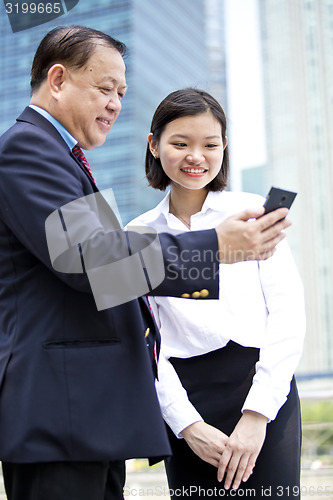 Image of Asian businessman and young female executive looking at smart phone