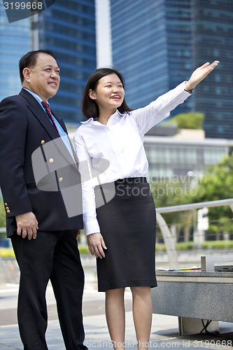 Image of Asian businessman and young female executive pointing at a direction