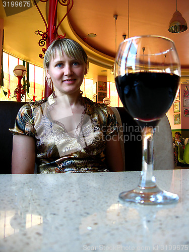 Image of glass of red wine on the table and a girl