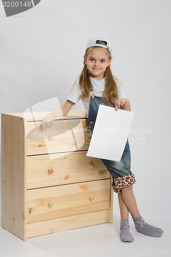 Image of Girl in overalls collector furniture near chest with a sheet of paper