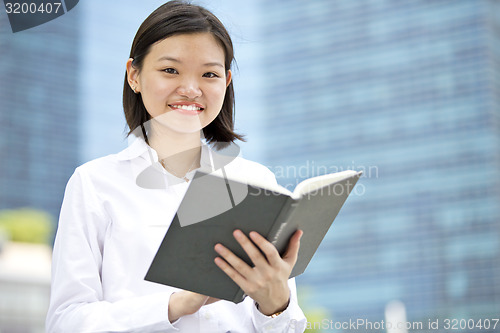 Image of Asian young female executive holding book smiling