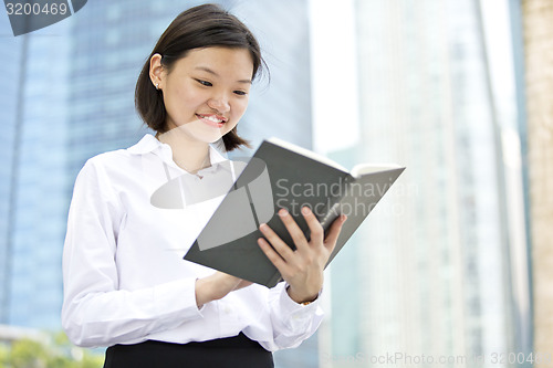 Image of Asian young female executive holding book smiling