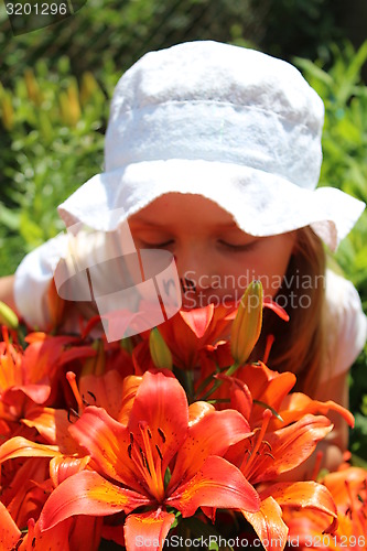 Image of little girl smells lilies on the flower-bed