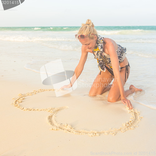 Image of Woman drawing heart on the sand.