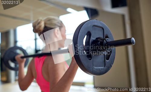 Image of happy woman flexing muscles with barbell in gym