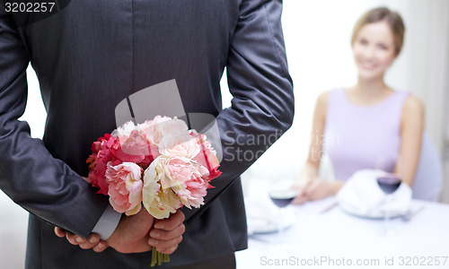 Image of close up of man hiding flowers behind from woman