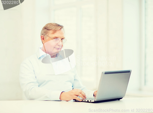 Image of old man in eyeglasses working with laptop at home