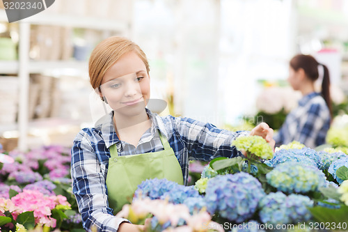 Image of happy woman taking care of flowers in greenhouse