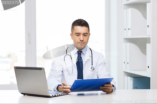 Image of male doctor with clipboard and laptop in office