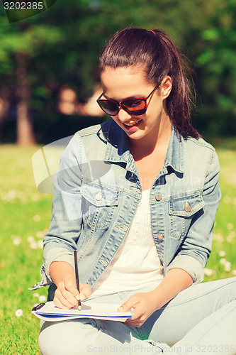 Image of smiling young girl with notebook writing in park