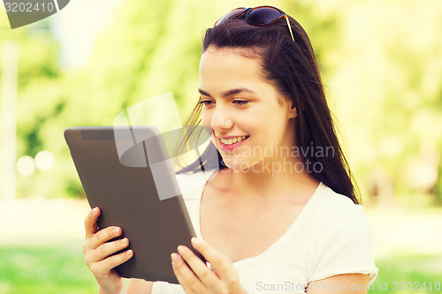 Image of smiling young girl with tablet pc sitting on grass