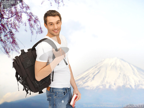 Image of happy young man with backpack and book travelling