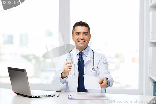 Image of smiling doctor with tablets and laptop in office