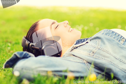 Image of smiling young girl in headphones lying on grass