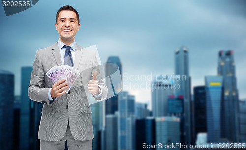 Image of smiling businessman with money showing thumbs up