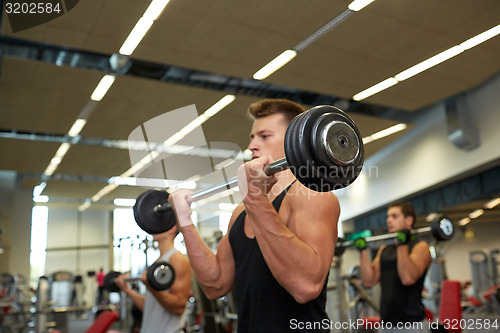Image of young men flexing muscles with barbells in gym
