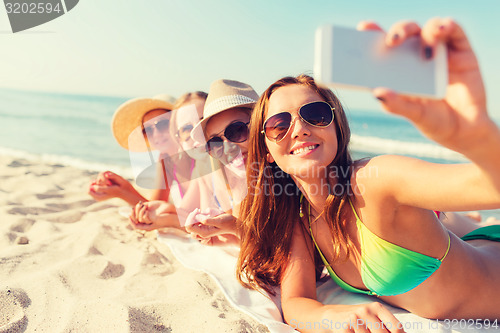 Image of group of smiling women with smartphone on beach