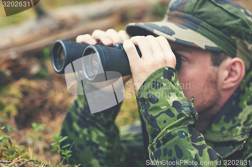 Image of young soldier or hunter with binocular in forest