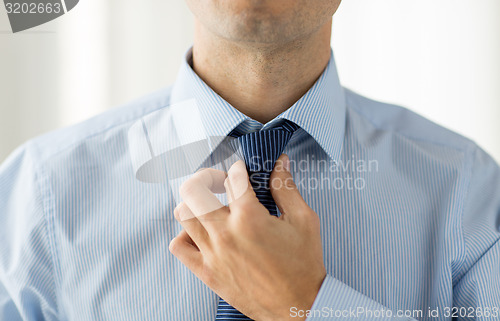 Image of close up of man in shirt adjusting tie on neck