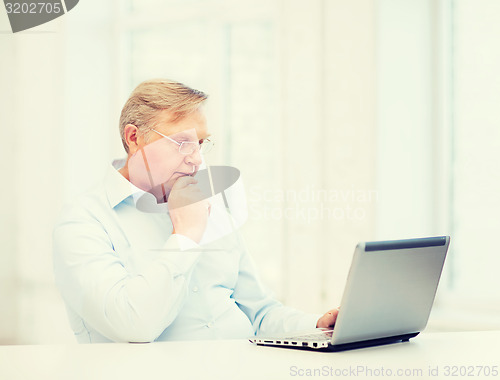 Image of old man in eyeglasses working with laptop at home