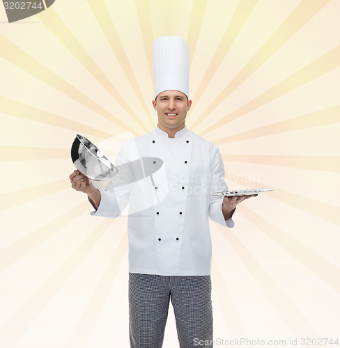 Image of happy male chef cook opening cloche