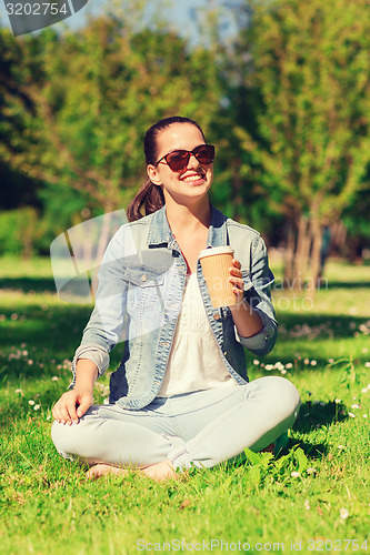 Image of smiling young girl with cup of coffee in park