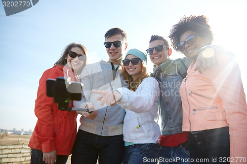 Image of smiling friends taking selfie with smartphone