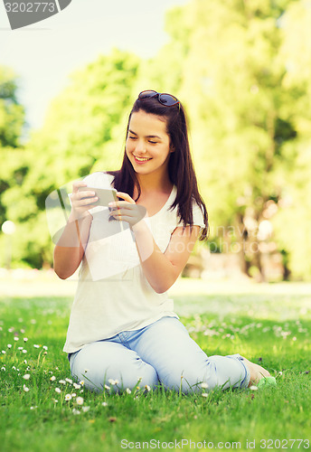 Image of smiling young girl with smartphone sitting in park