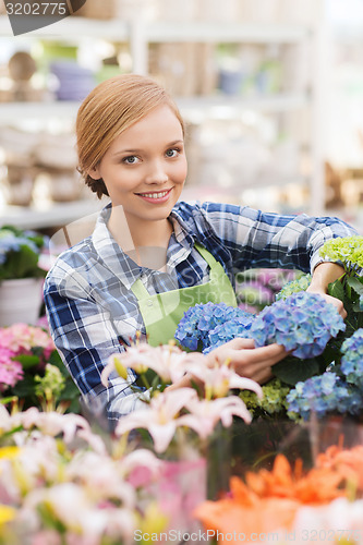 Image of happy woman taking care of flowers in greenhouse