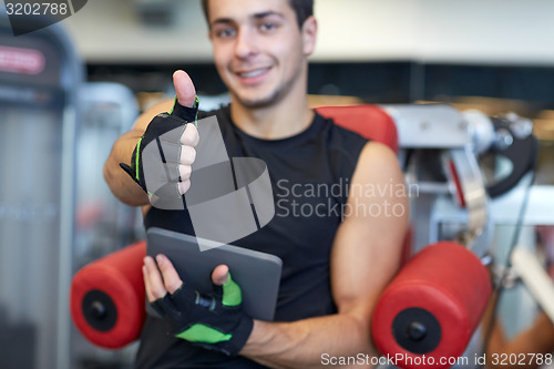 Image of young man with tablet pc showing thumbs up in gym