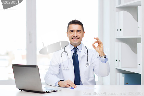 Image of smiling doctor with laptop showing ok in office