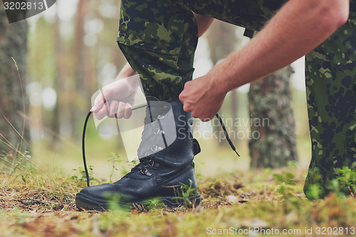 Image of close up of soldier tying bootlaces in forest