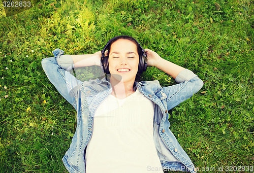 Image of smiling young girl in headphones lying on grass