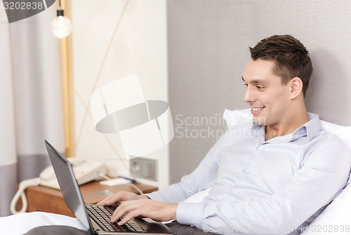 Image of happy businesswoman with laptop in hotel room