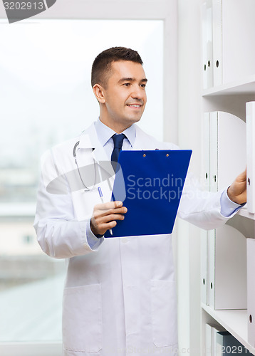 Image of happy doctor with clipboard in medical office