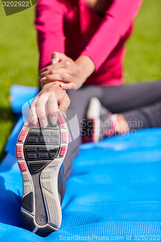 Image of close up of woman stretching leg on mat outdoors