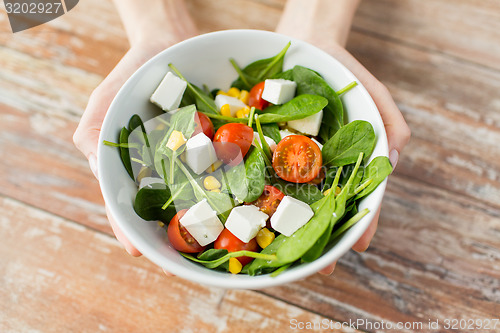 Image of close up of young woman hands showing salad bowl