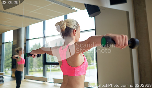 Image of woman with dumbbells flexing muscles in gym