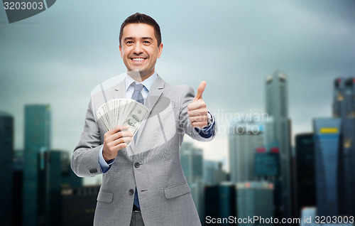 Image of smiling businessman with money showing thumbs up