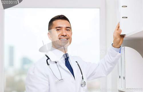 Image of happy doctor with clipboard in medical office