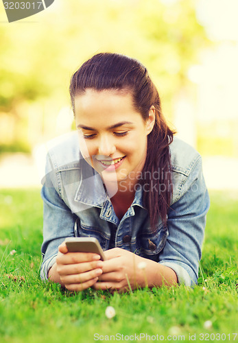 Image of smiling young girl with smartphone lying on grass