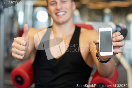 Image of young man with smartphone showing thumbs up in gym