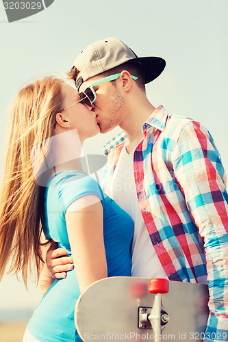 Image of smiling couple with skateboard kissing outdoors