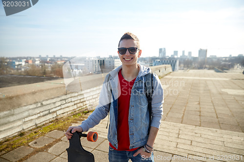 Image of smiling man or teenager with longboard on street