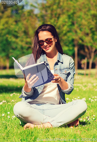 Image of smiling young girl with book sitting in park