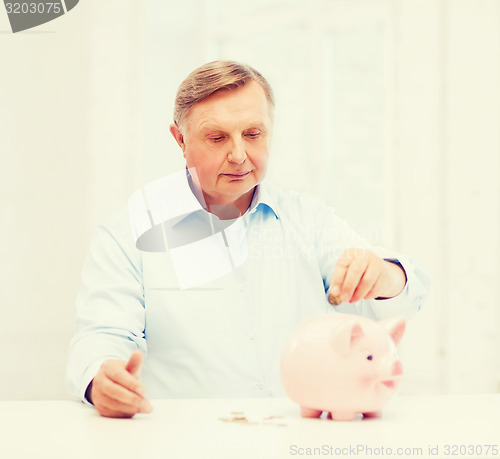 Image of old man putting coin into big piggy bank