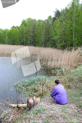 Image of fisherman beside forest lake