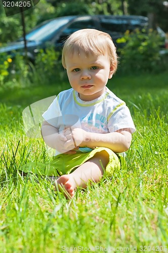 Image of Little boy in the summer park sitting on the grass