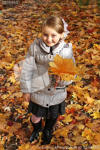 Image of little girl with yellow leaf in autumn