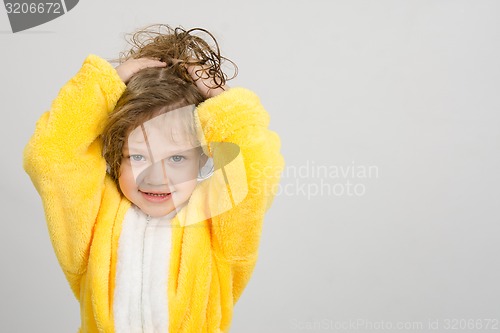 Image of Cheerful girl in yellow bathrobe holding hair